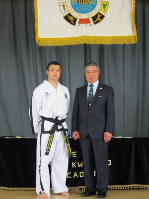 Mr Johnnie Chan standing next to First Taekwon-Do Grandmaster Rhee Ki Ha following a black belt promotion. They are standing in front of the Taekwon-Do examination table and ITF plaque flag