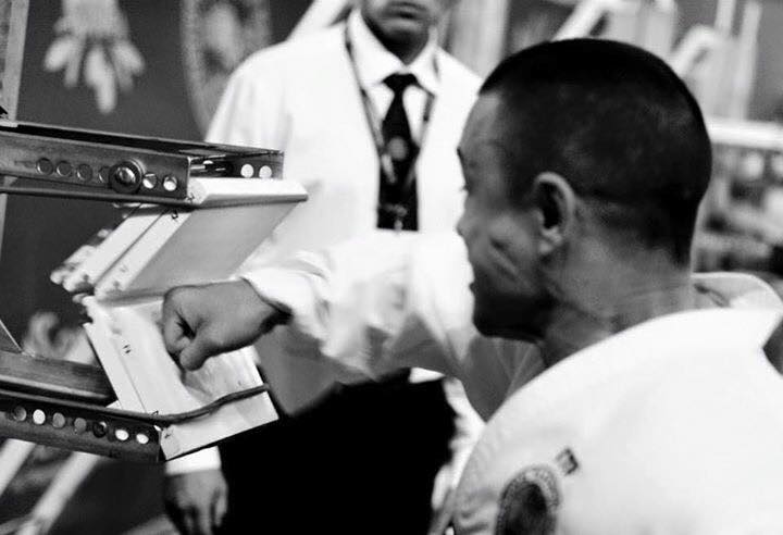Mr Jonny Chan VI punching two white boards at a martial art competition. The boards are mid break and you can see the effort in his face. Black and white image