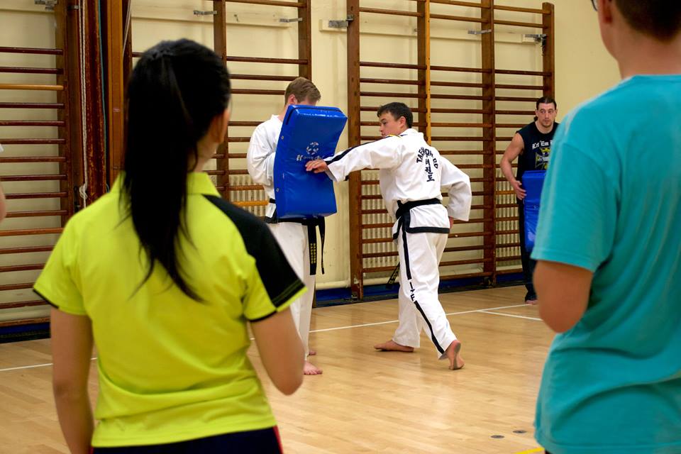 Mr Chan teaching Taekwon-Do to new students. Black belt holding a pad shield while Mr Chan performs a reverse knife hand strike.
