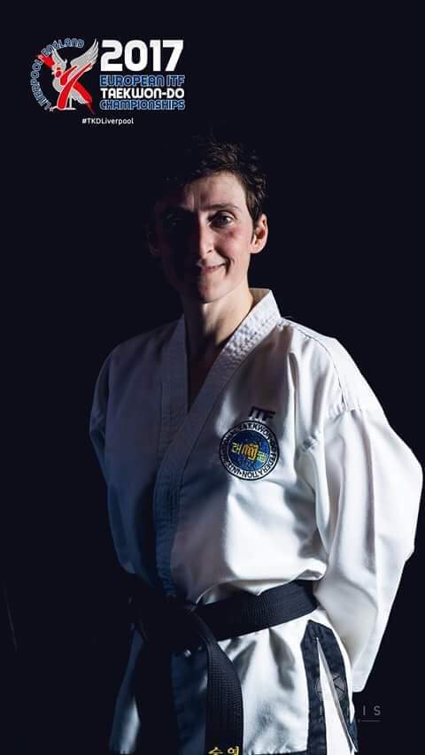 Promotional photograph of Eddie Dobson IV dan wearing dobok - presenting the Liverpool European Championships 2017 logo. Dark background with strong light contrast.