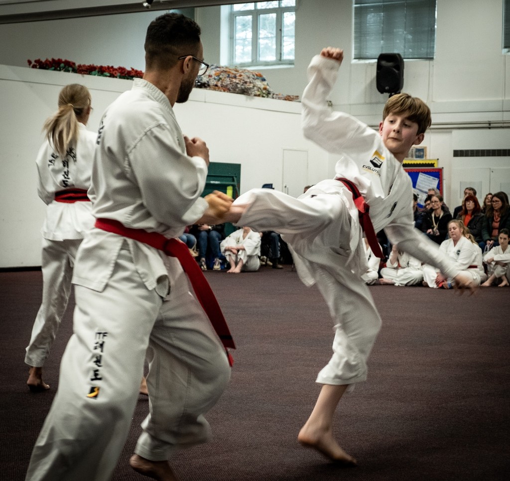 Two red belts sparring in a seminar with others sitting and watching. Possibly a black belt grading